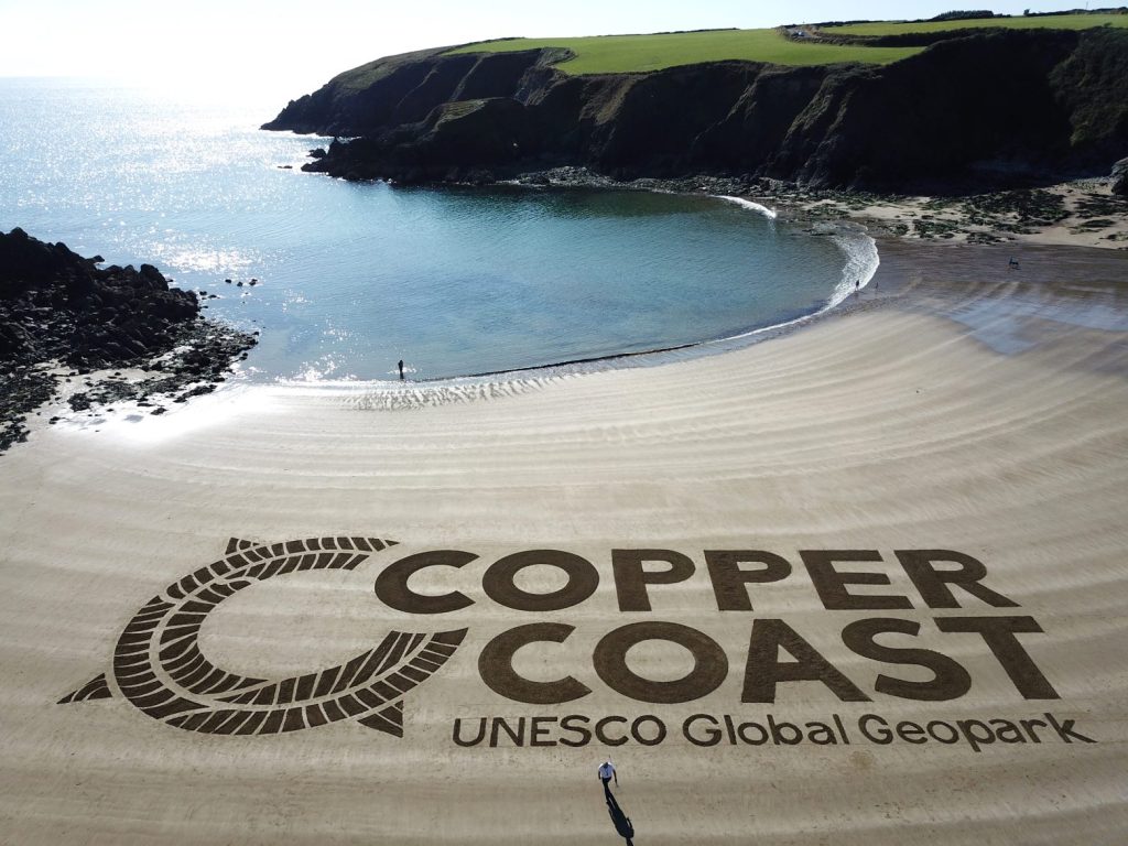 Copper Coast Geopark logo in the sand at Kilmurran Cove.
